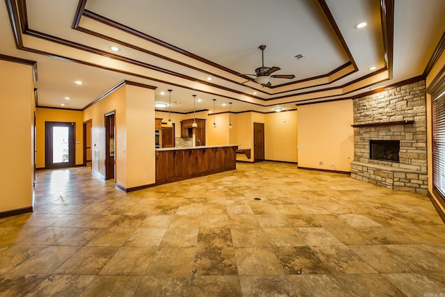 unfurnished living room featuring baseboards, visible vents, a ceiling fan, a tray ceiling, and a stone fireplace