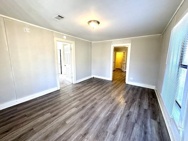 spare room with dark wood-type flooring, visible vents, crown molding, and baseboards