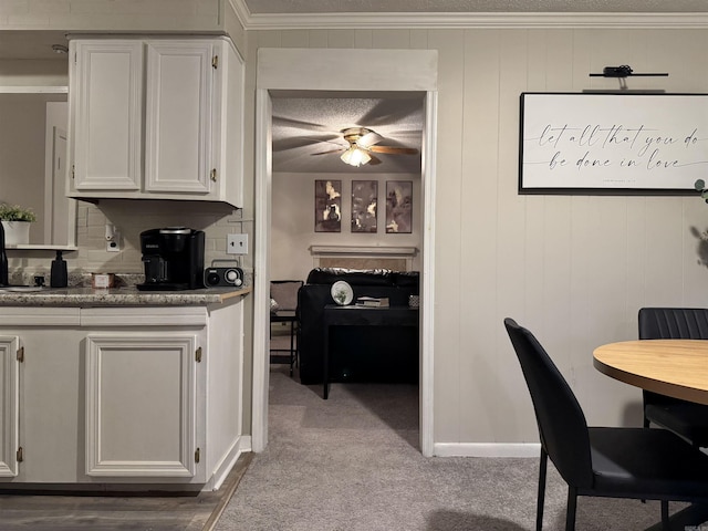 kitchen with ceiling fan, ornamental molding, carpet, white cabinetry, and backsplash