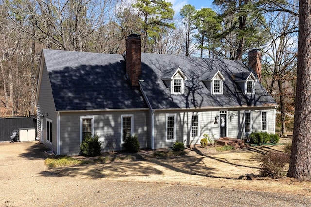 cape cod house featuring roof with shingles, a chimney, and dirt driveway