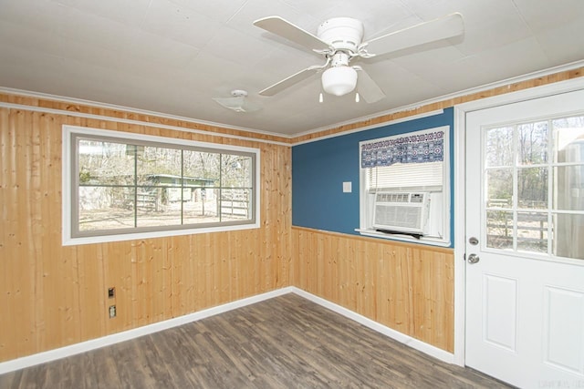 empty room with wood walls, dark wood finished floors, a ceiling fan, and baseboards