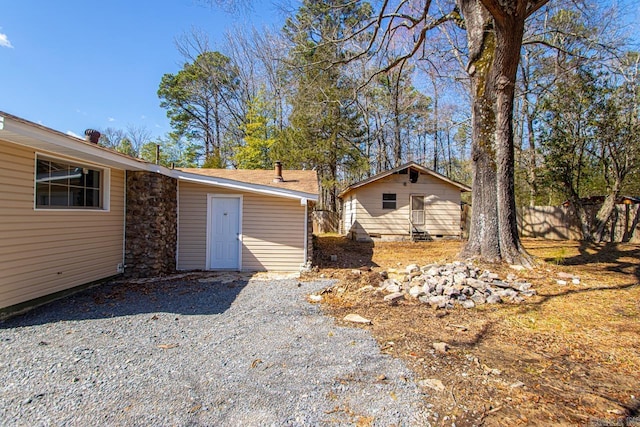 rear view of property with gravel driveway, fence, and an outdoor structure