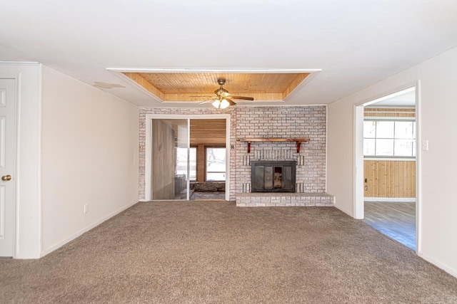 unfurnished living room with carpet, a tray ceiling, plenty of natural light, and a brick fireplace