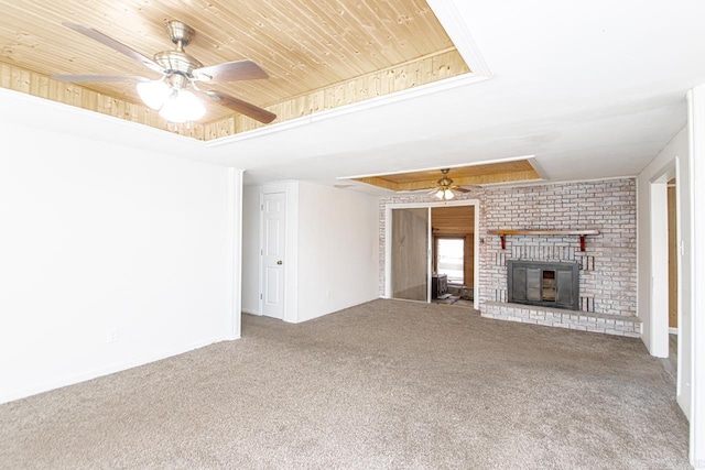 unfurnished living room with carpet flooring, wood ceiling, a ceiling fan, a brick fireplace, and a tray ceiling