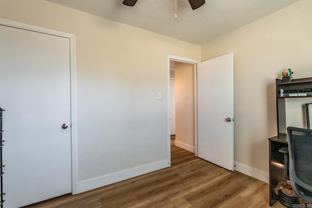 unfurnished bedroom with ceiling fan, a textured ceiling, baseboards, and wood finished floors