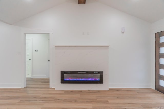 unfurnished living room with heating unit, light wood-style flooring, a glass covered fireplace, vaulted ceiling, and baseboards