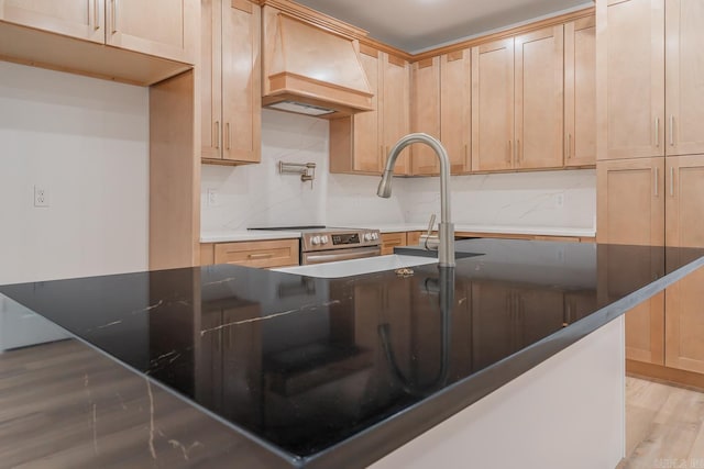 kitchen featuring light wood-style floors, light brown cabinetry, tasteful backsplash, stainless steel range with electric stovetop, and custom range hood