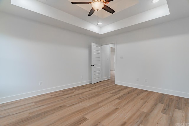 empty room featuring baseboards, a ceiling fan, a tray ceiling, light wood-type flooring, and recessed lighting