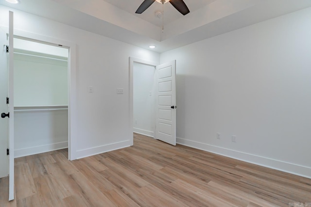 unfurnished bedroom featuring light wood-style floors, a tray ceiling, baseboards, and recessed lighting