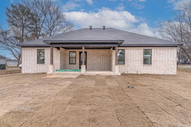 rear view of property featuring brick siding, roof with shingles, and a porch