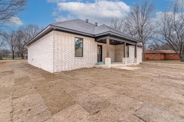 back of house with brick siding and a shingled roof