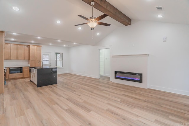 living area with vaulted ceiling with beams, visible vents, a glass covered fireplace, ceiling fan, and light wood-type flooring