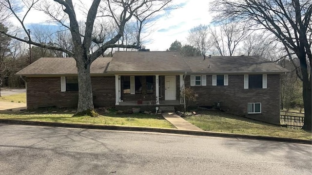 ranch-style house with brick siding, roof with shingles, a porch, and a front yard