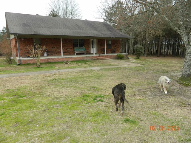 view of front facade with roof with shingles, a front lawn, a porch, and brick siding