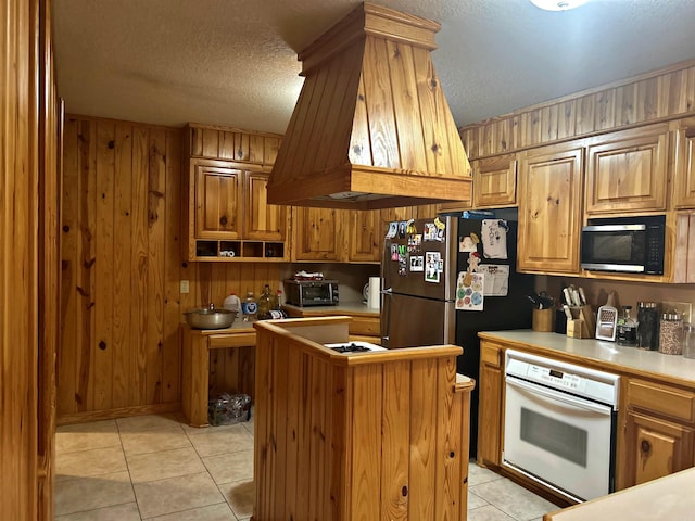 kitchen with a center island, white oven, light tile patterned flooring, black microwave, and premium range hood