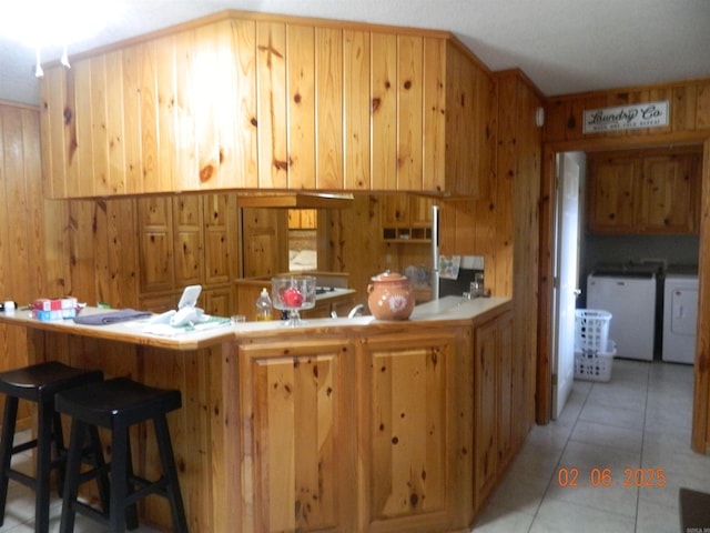 kitchen with light tile patterned floors, a peninsula, wood walls, and washing machine and dryer