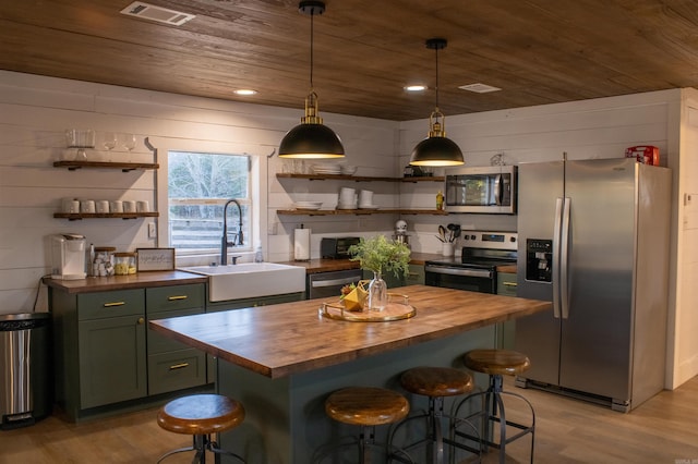 kitchen with green cabinets, butcher block countertops, a sink, and appliances with stainless steel finishes