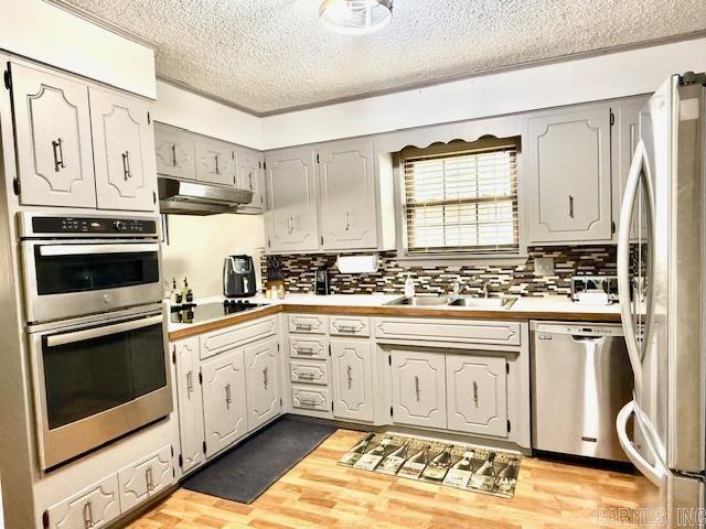 kitchen featuring light countertops, appliances with stainless steel finishes, light wood-style floors, a sink, and under cabinet range hood