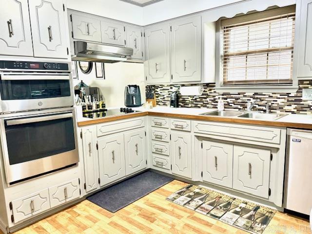 kitchen with double oven, white dishwasher, black electric cooktop, under cabinet range hood, and a sink