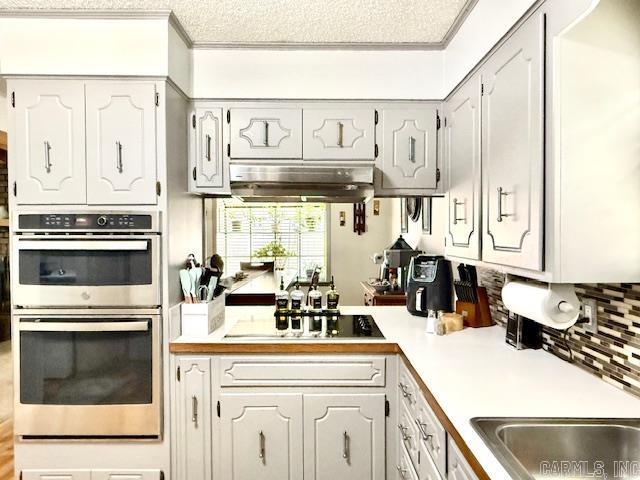 kitchen with double oven, light countertops, black cooktop, and under cabinet range hood