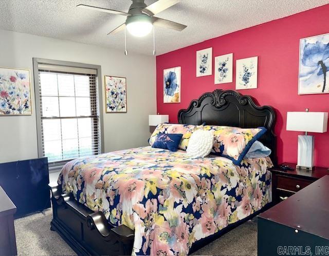 carpeted bedroom featuring an accent wall, a textured ceiling, and a ceiling fan