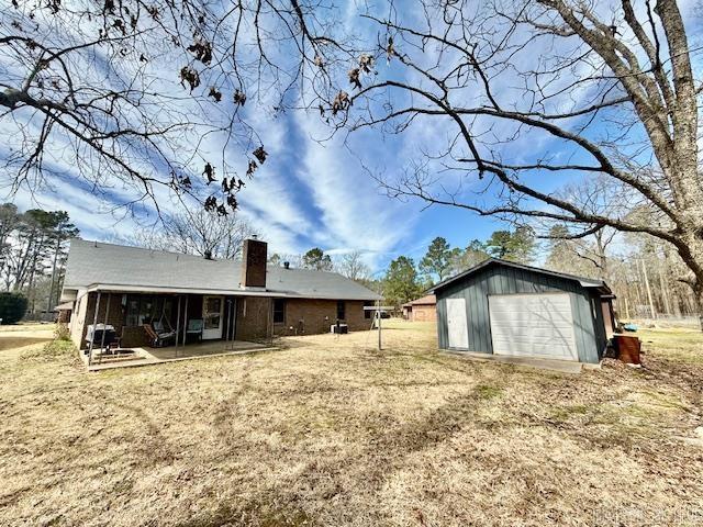 rear view of house with an outbuilding, a garage, dirt driveway, a chimney, and a patio area