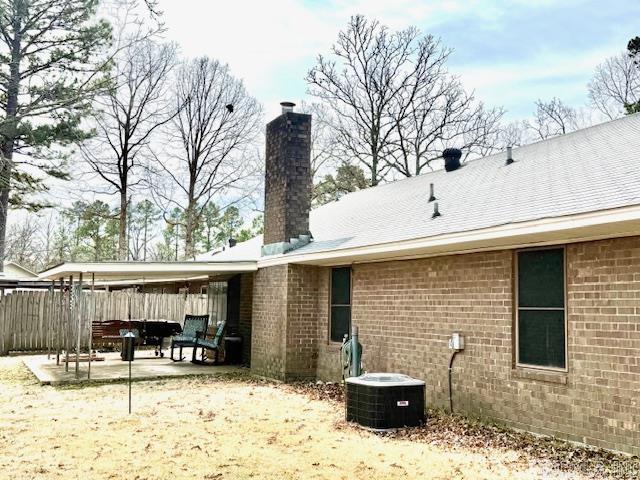 back of property with central air condition unit, brick siding, fence, a chimney, and a patio area