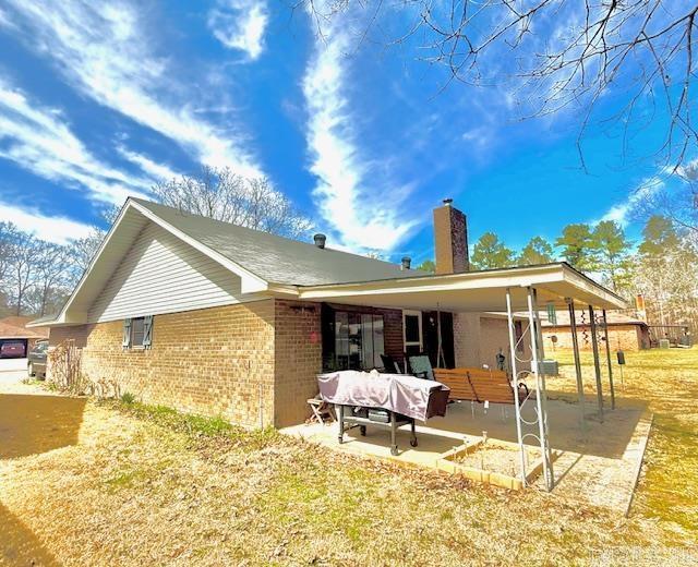 rear view of property with a patio, brick siding, and a chimney