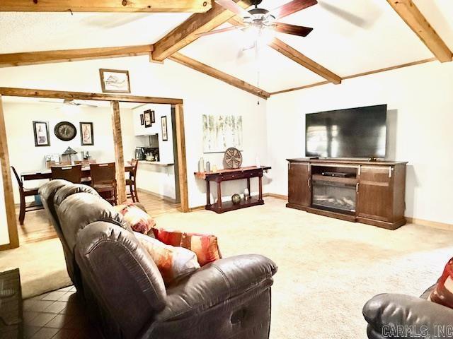 carpeted living room featuring lofted ceiling with beams, ceiling fan, baseboards, and a glass covered fireplace