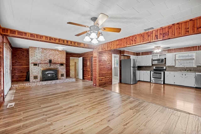 unfurnished living room with a fireplace, light wood finished floors, a ceiling fan, a sink, and wooden walls