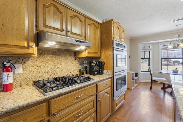 kitchen featuring stainless steel appliances, brown cabinets, visible vents, and under cabinet range hood