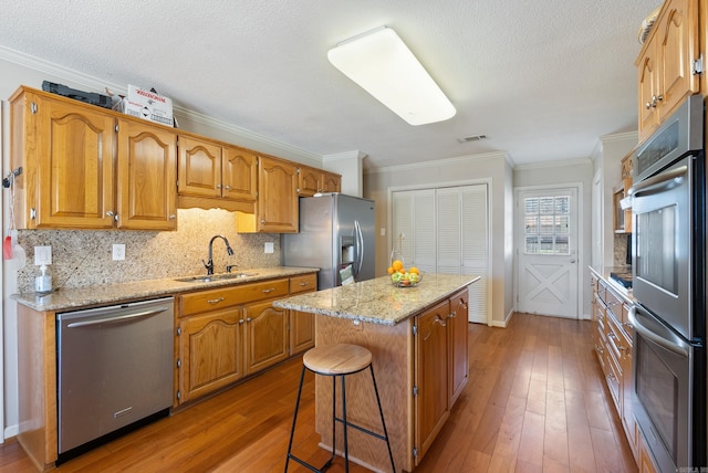 kitchen featuring light wood-style flooring, appliances with stainless steel finishes, ornamental molding, a center island, and a sink