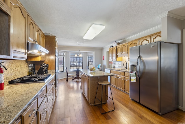 kitchen featuring hardwood / wood-style flooring, ornamental molding, stainless steel appliances, under cabinet range hood, and a sink