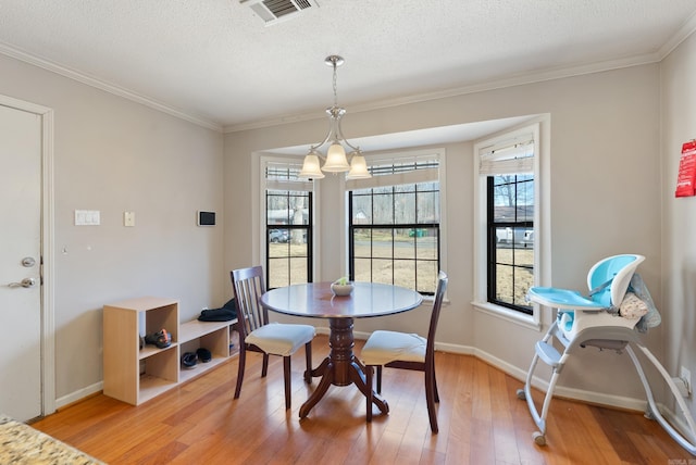 dining space featuring light wood-type flooring, a textured ceiling, visible vents, and crown molding