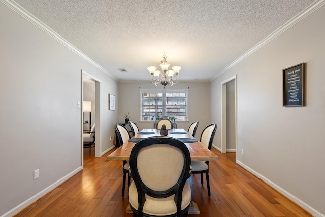 dining room featuring light wood finished floors, baseboards, visible vents, an inviting chandelier, and crown molding