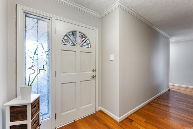 foyer entrance with a textured ceiling, ornamental molding, wood finished floors, and baseboards