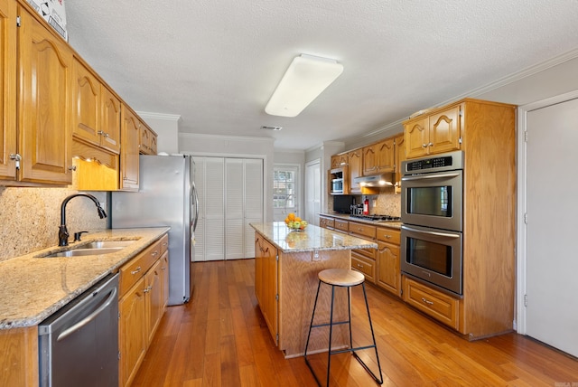 kitchen featuring a kitchen island, appliances with stainless steel finishes, light stone counters, under cabinet range hood, and a sink