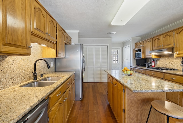 kitchen with appliances with stainless steel finishes, ornamental molding, a sink, a kitchen island, and under cabinet range hood