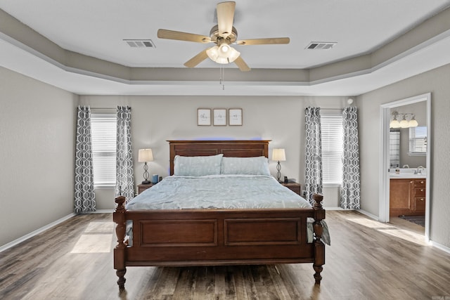 bedroom with a tray ceiling, visible vents, and wood finished floors