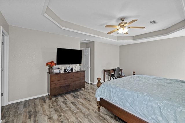 bedroom with baseboards, visible vents, a raised ceiling, and wood finished floors