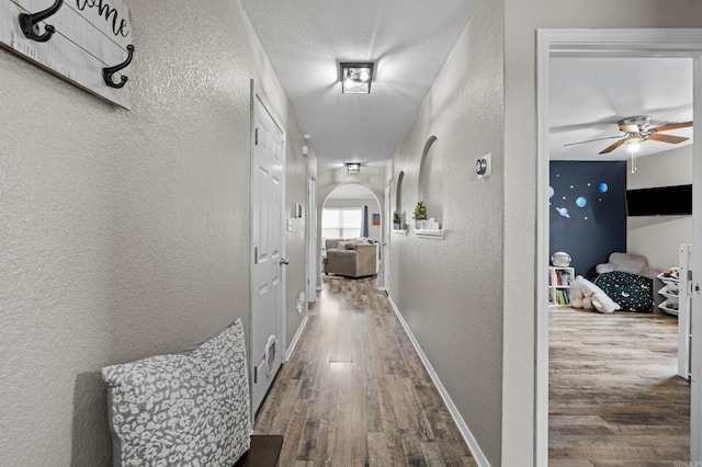 hall with arched walkways, a textured wall, and wood finished floors