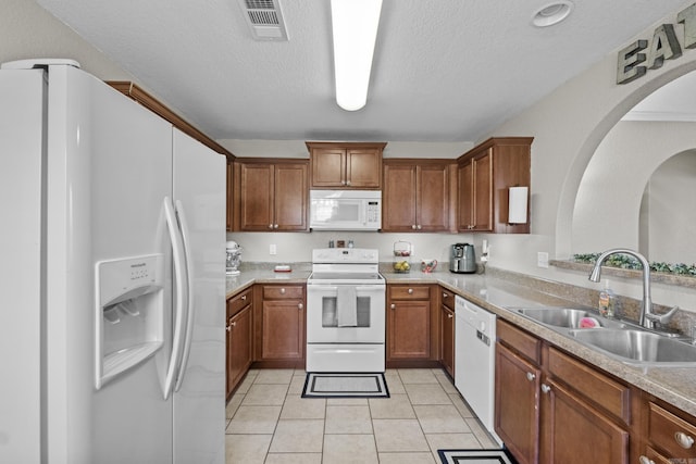 kitchen featuring white appliances, a sink, visible vents, and brown cabinets