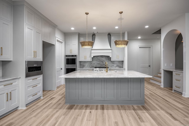 kitchen featuring double oven, custom range hood, light wood-style floors, and gray cabinetry