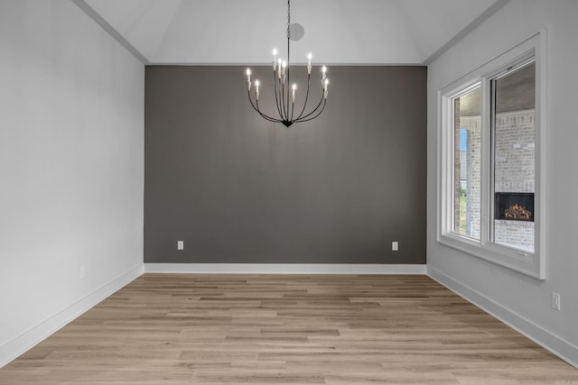 empty room with a chandelier, vaulted ceiling, light wood-style flooring, and baseboards