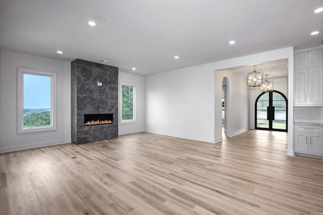 unfurnished living room featuring arched walkways, baseboards, a high end fireplace, light wood-type flooring, and recessed lighting