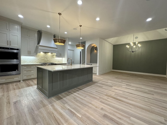 kitchen featuring arched walkways, stainless steel double oven, premium range hood, a sink, and gray cabinets