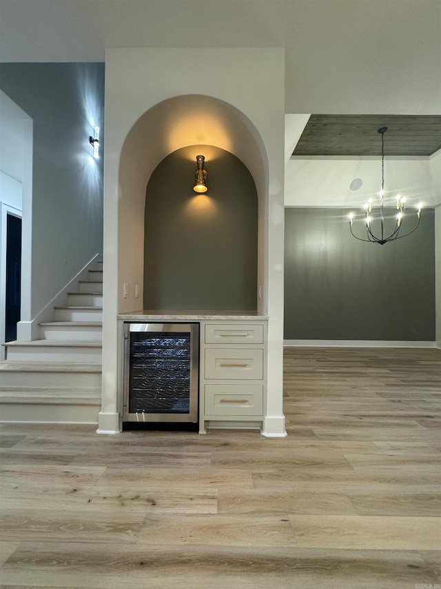 interior space featuring wine cooler, stairway, an inviting chandelier, a bar, and light wood-style floors