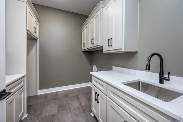 clothes washing area featuring washer hookup, cabinet space, a sink, dark tile patterned flooring, and baseboards