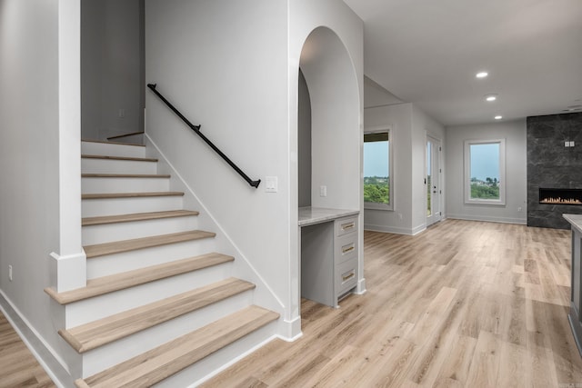 staircase with baseboards, arched walkways, wood finished floors, a fireplace, and recessed lighting