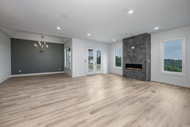 unfurnished living room with a high end fireplace, recessed lighting, light wood finished floors, and an inviting chandelier